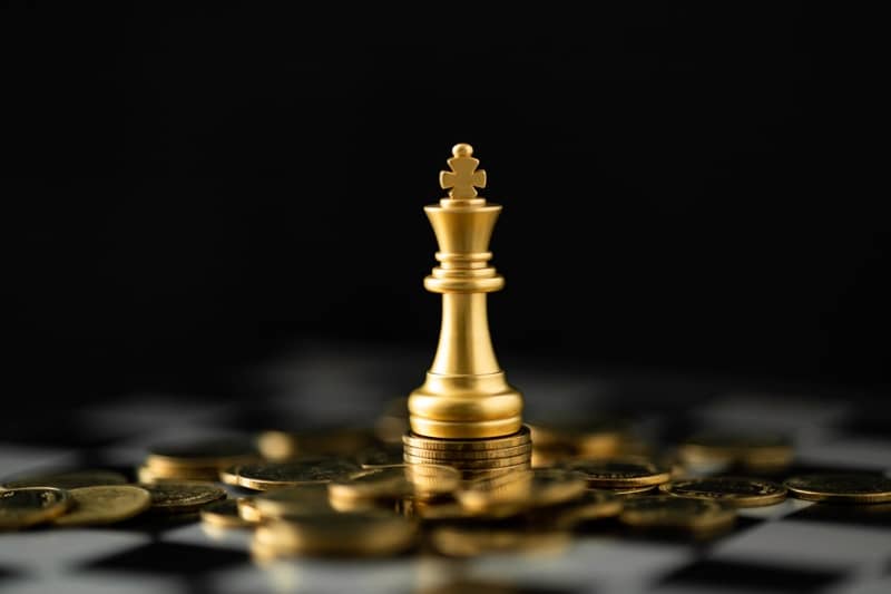 Chess king piece surrounded by stacked coins on a chessboard representing strategic real estate funding